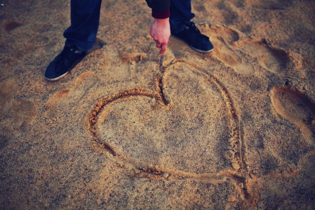 man drawing heart with a stick in sand